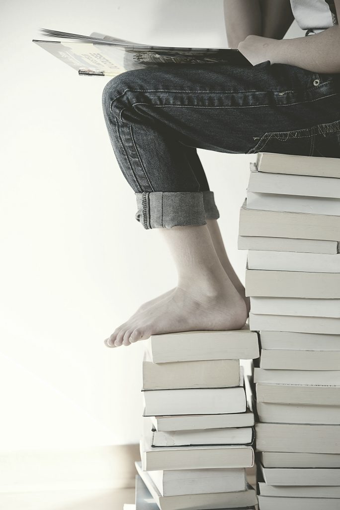 Legs and feed of a person sitting on a stack of books